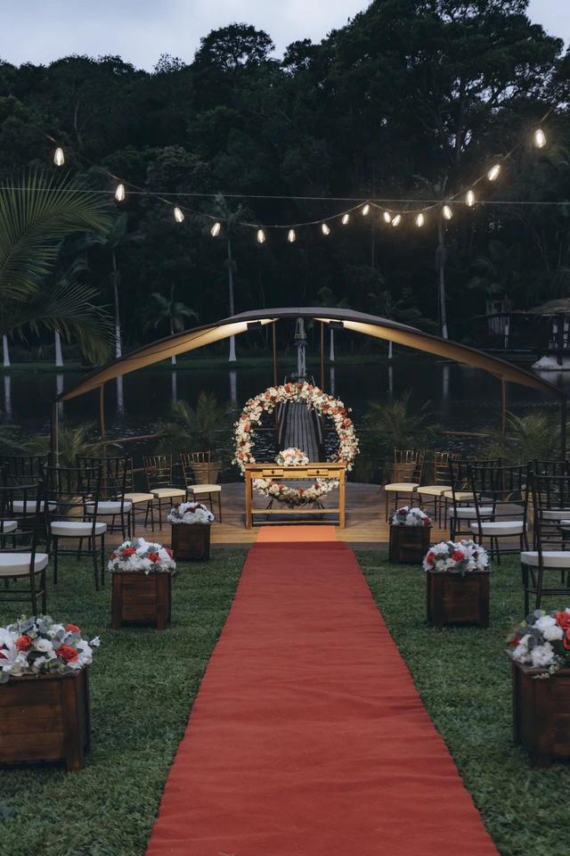 Altar com arco de flores e tapete vermelho iluminado ao anoitecer