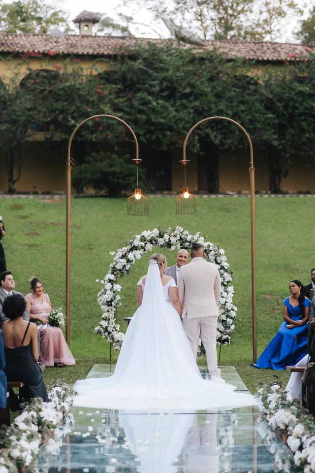 Noivos diante do altar com arco de flores em uma cerimônia ao ar livre